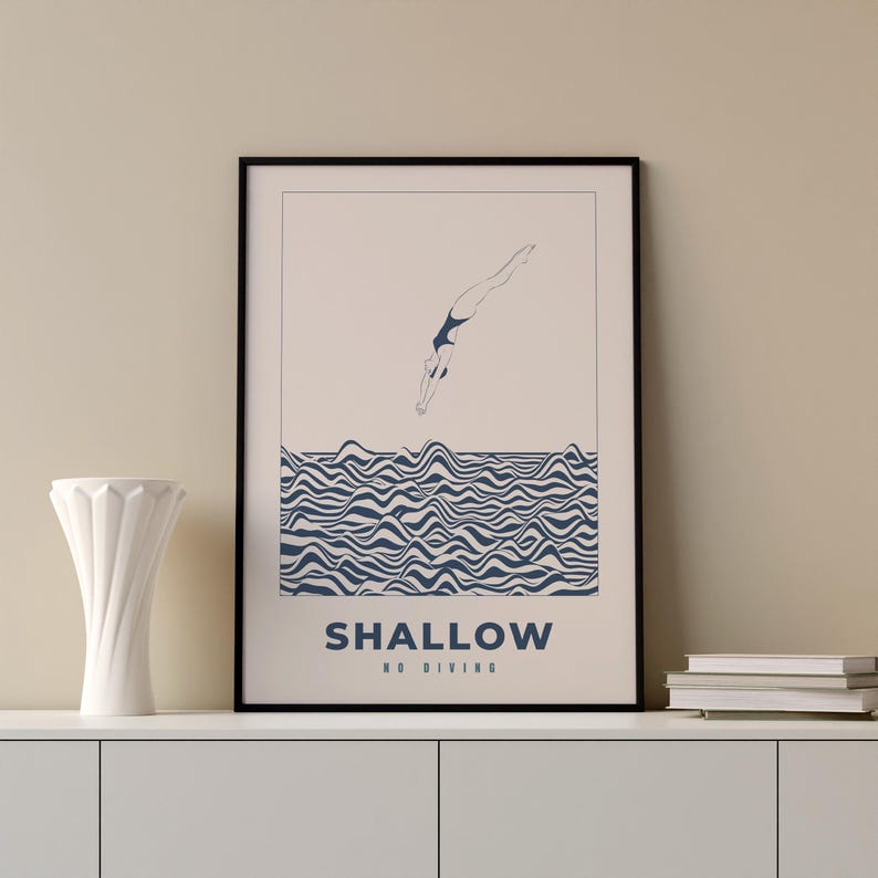 Op de afbeelding: Een zwart ingelijste poster met een witte achtergrond en een blauwe illustratie van een persoon die in golvend water duikt. De tekst "SHALLOW NO DIVING" staat onderaan de poster.
