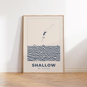 Op de afbeelding: Een ingelijste poster met een minimalistische illustratie van een persoon die in een golvende zee duikt. De poster heeft de tekst "SHALLOW NO DIVING" in blauw.
