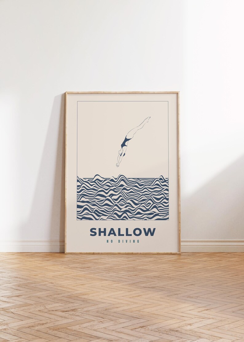 Op de afbeelding: Een ingelijste poster met een minimalistische illustratie van een persoon die in een golvende zee duikt. De poster heeft de tekst "SHALLOW NO DIVING" in blauw.