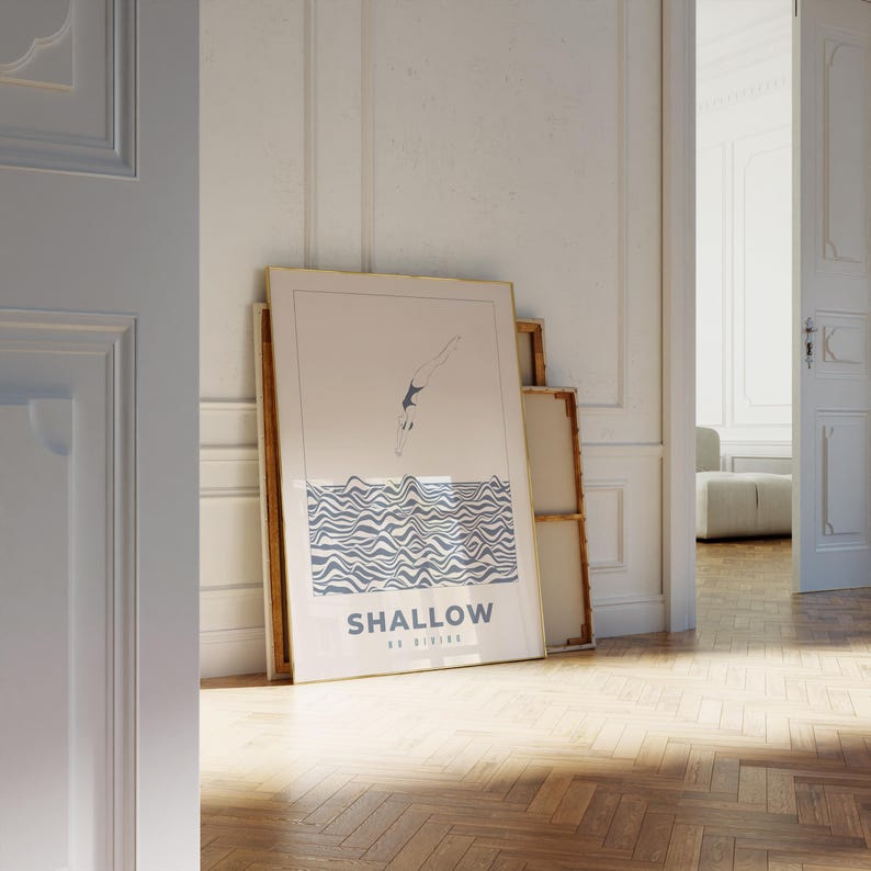 Op de afbeelding: Een ingelijste print met een minimalistische illustratie van een persoon die in golvend water duikt. De print is in een gouden lijst en heeft de tekst "SHALLOW NO DIVING" onderaan.