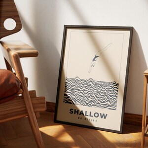 Op de afbeelding: Een zwart ingelijste poster met een beige achtergrond waarop een lijntekening van een persoon te zien is die in golvend zwart-wit water duikt. De tekst "SHALLOW NO DIVING" is in zwart onderaan de poster gedrukt.