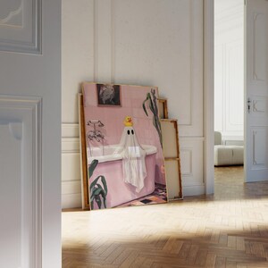 K&ouml;nnte beinhalten: Ein gerahmtes Kunstwerk zeigt einen Geist in einer Badewanne, der eine gelbe Quietscheente auf dem Kopf tr&auml;gt. Das rosa Badezimmer hat eine wei&szlig;e Badewanne und einen schwarz-wei&szlig; gefliesten Boden. Gr&uuml;ne Pflanzen und ein gerahmtes Bild sind ebenfalls zu sehen.