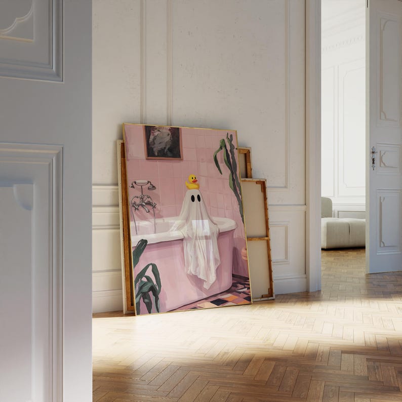 K&ouml;nnte beinhalten: Ein gerahmtes Kunstwerk zeigt einen Geist in einer Badewanne, der eine gelbe Quietscheente auf dem Kopf tr&auml;gt. Das rosa Badezimmer hat eine wei&szlig;e Badewanne und einen schwarz-wei&szlig; gefliesten Boden. Gr&uuml;ne Pflanzen und ein gerahmtes Bild sind ebenfalls zu sehen.