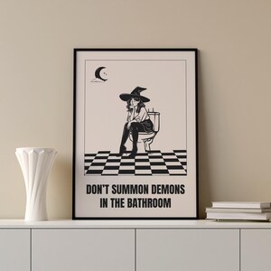 Peut inclure: Illustration en noir et blanc d'une sorci&egrave;re assise sur des toilettes avec le texte "Ne pas invoquer des d&eacute;mons dans la salle de bain".