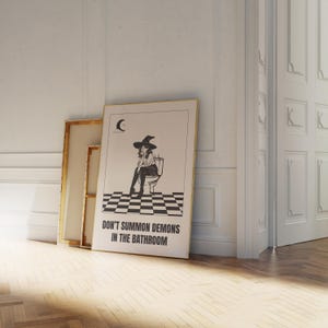 Peut inclure: Une illustration en noir et blanc d'une sorci&egrave;re assise sur des toilettes avec une lune croissante en arri&egrave;re-plan. Le texte "Ne pas invoquer des d&eacute;mons dans la salle de bain" est sous l'image.