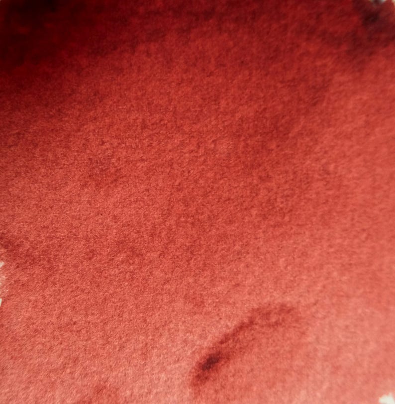 May include: Close-up of a textured, reddish-brown surface. The color appears to be a deep, warm tone, with subtle variations in shade across the surface. The texture is soft and slightly uneven, suggesting a fabric or felt-like material.