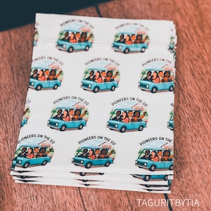 May include: A stack of white fabric with a repeating pattern of a light blue van with people inside and the text "Pioneers on the Go." The van design includes a house and a waving arm. The fabric is on a wooden surface.