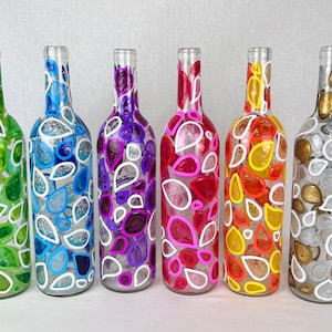 May include: Six glass wine bottles painted with white outlines of teardrop shapes. Each bottle is a different color: green, blue, purple, pink, orange, and gold.