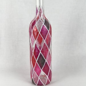 May include: A clear glass bottle with a diamond pattern painted in shades of pink, red, and white. The bottle has a silver glitter accent.