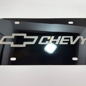 Puede incluir: Placa de matrícula negra con un logotipo de Chevy plateado y la palabra "CHEVY" en letras plateadas.