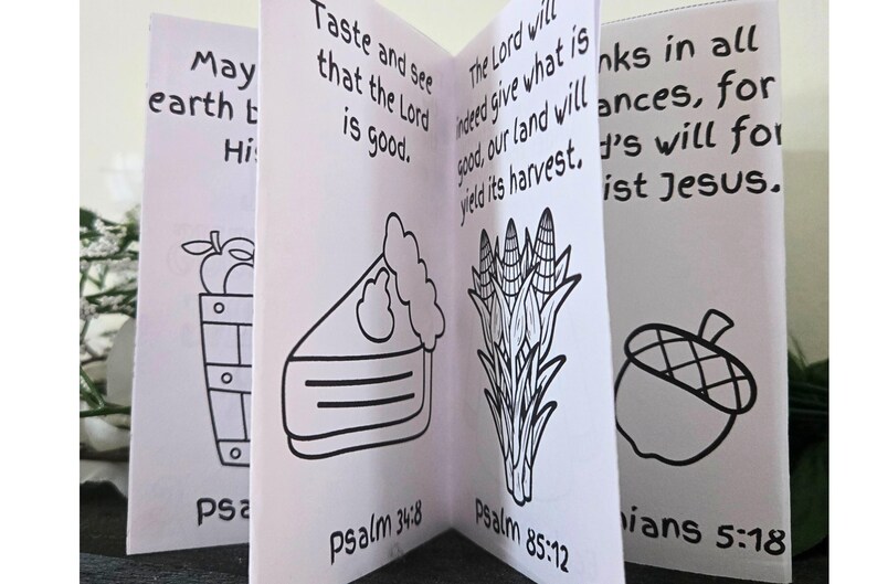 May include: A small, open book with black line drawings and text. The illustrations include a basket of apples, a slice of pie, corn stalks, and an acorn. Text includes Bible verses like "Taste and see that the Lord is good."