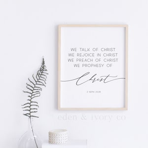 Puede incluir: Una impresión enmarcada con fondo blanco y texto negro. El texto dice "We talk of Christ, We rejoice in Christ, We preach of Christ, We prophesy of Christ" con la referencia bíblica "2 Nephi 25:26". La impresión está sobre un escritorio blanco con un jarrón de helechos, una pila de libros y un par de gafas.