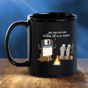 May include: Black ceramic mug with a humorous graphic featuring a floppy disk and USB drives around a campfire, with the text "...AND THEN YOU'D HAVE TO DIAL UP TO GET INTERNET."