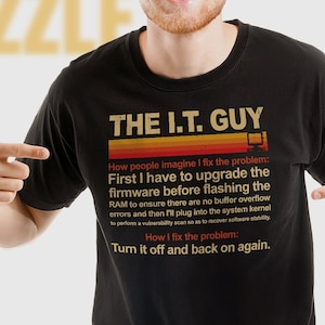 Könnte beinhalten: Ein schwarzes Unisex-T-Shirt mit einem Retro-Grafikdesign. Der Text lautet "The I.T. Guy" und beschreibt, wie Leute sich vorstellen, wie Probleme behoben werden, und wie sie tatsächlich behoben werden. Der Text lautet "Wie Leute sich vorstellen, dass ich das Problem löse: Zuerst muss ich die Firmware aktualisieren, bevor ich den RAM flashe, um sicherzustellen, dass keine Pufferüberläufe auftreten, und dann stecke ich den Systemkern ein. Wie ich das Problem löse: Schalte es aus und wieder ein."