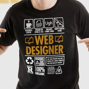 Può includere: Maglietta nera con un design grafico bianco che recita "Web Designer" con un elenco di requisiti, avvertenze e precauzioni. La grafica è in stile etichetta di prodotto.