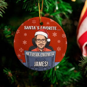 Könnte beinhalten: Ein runder Weihnachtsschmuck mit rotem Hintergrund und einer Cartoon-Zeichnung eines Mannes mit Weihnachtsmütze. Der Text lautet "SANTA'S FAVORITE... NETWORK ENGINEER JAMES!". Der Schmuck hängt an einem Weihnachtsbaum.