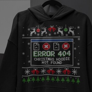 Może przedstawiać: Czarna bluza z kapturem z nadrukiem okna błędu komputera z tekstem ERROR 404 CHRISTMAS HOODIE NOT FOUND. Wzór zawiera pikselowe renifery, czerwone i zielone ozdoby, dzwonki, płatki śniegu oraz zielone drzewka iglaste rozmieszczone w rzędach.