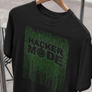 Könnte beinhalten: Schwarzes T-Shirt mit einer grünen Grafik, auf der "Hacker Mode" mit einem Power-Knopf-Symbol steht.