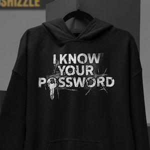 May include: A black long-sleeve hooded sweatshirt featuring a white graphic print on the chest. The text reads I KNOW YOUR PASSWORD, with the letter O in PASSWORD replaced by a key icon. The design has a distressed, weathered texture.