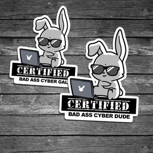 May include: Two black and white stickers with a cartoon bunny wearing sunglasses and using a laptop. The text on the stickers reads "CERTIFIED BAD ASS CYBER GAL" and "CERTIFIED BAD ASS CYBER DUDE".