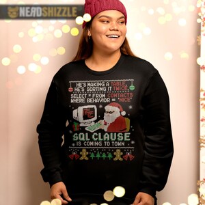 K&ouml;nnte beinhalten: Ein schwarzes Langarm-Sweatshirt mit einem Grafikdruck von Santa Claus an einem Computer. Der Text lautet: He's making a table, he's sorting it twice, select * from contacts where behavior = 'nice', SQL clause is coming to town.