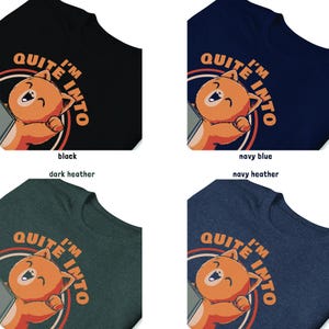 Puede incluir: Cuatro camisetas en negro, azul marino, gris oscuro y azul marino jaspeado. Cada camiseta presenta un dibujo de gato de dibujos animados con el texto "I'M QUITE INTO" en un dise&ntilde;o circular. El gato es naranja con vientre blanco y expresi&oacute;n feliz.