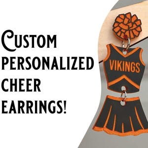 May include: A pair of custom cheer earrings with a black and orange pom-pom, a black and orange cheer uniform top with the word "VIKINGS" on the front, and a black and orange cheer skirt.