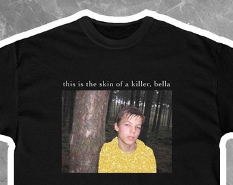 May include: Black t-shirt with a graphic print of a young person in a yellow shirt standing in a forest. The text "this is the skin of a killer, bella" is printed above the graphic.