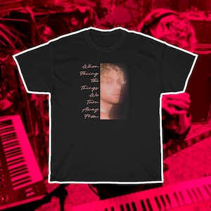 May include: Black t-shirt featuring a photograph of a man and the text "When Facing the Things We Turn Away From" in pink.