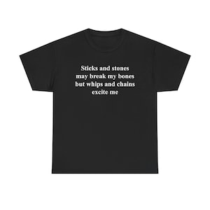 Puede incluir: Camiseta negra con texto blanco: "Palos y piedras pueden romper mis huesos, pero los látigos y las cadenas me excitan." La camiseta tiene cuello redondo y mangas cortas. El texto está centrado en la parte delantera.