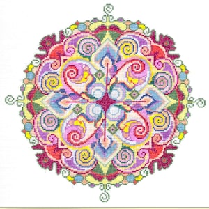 Op de afbeelding: Een kleurrijk kruissteek mandala-ontwerp. Het cirkelvormige patroon heeft een symmetrische opstelling van wervelende vormen in roze, paars, geel, blauw en groen. Het ontwerp is geplaatst tegen een witte achtergrond, met een decoratieve rand.