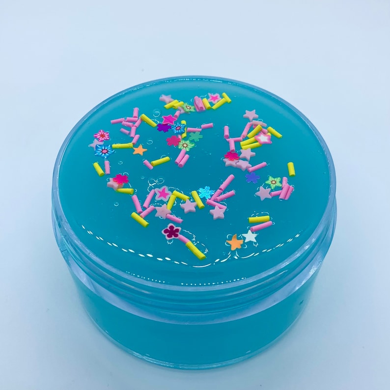 May include: A clear plastic container filled with light blue slime with pink, yellow, and white sprinkles.