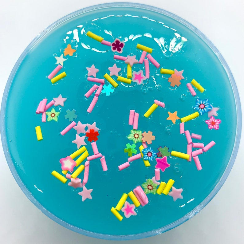 May include: A close-up of a blue slime with pink and yellow sprinkles. The slime is in a clear plastic container.