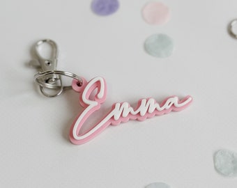 Puede incluir: Llavero de acrílico rosa con el nombre "Emma" escrito en letras blancas.