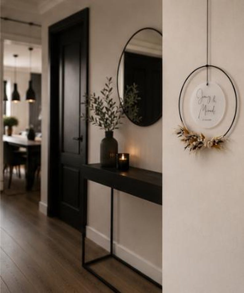May include: A circular black metal hoop wall hanging featuring a white acrylic disc with the text "Joey & Mared" and a date, accented with a cluster of dried beige and white flowers and grasses attached to the bottom of the ring.