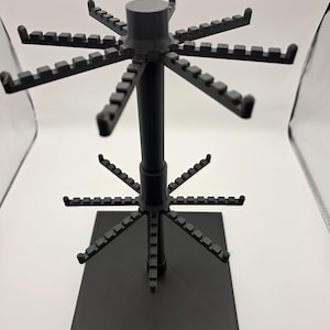 May include: A black rotating display stand with multiple arms extending outwards. Each arm has small notches for hanging items. The stand has a square base and a central pole. The design is modern and functional.