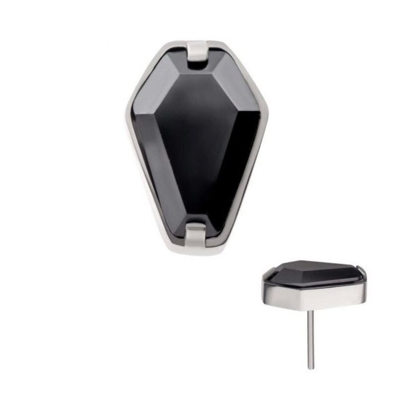May include: Black gemstone set in a silver-toned, faceted, coffin-shaped setting. The gemstone is a dark, opaque black. The setting is a simple, sleek design.