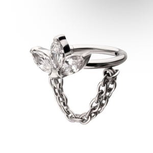 May include: A silver-colored piercing ring with a floral design and a dangling chain. The floral design features three clear, marquise-cut stones. The chain is made of small, interconnected links.