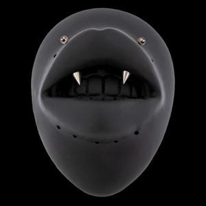 Peut inclure: Un masque noir brillant avec une large bouche ouverte, deux crocs argentés et de petits clous argentés près des yeux. Le masque a une forme lisse et arrondie avec de petits trous de ventilation.