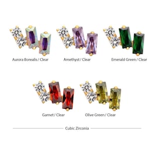May include: A collection of gold-toned jewelry pieces featuring rectangular and round cubic zirconia stones in various colors. The colors include Aurora Borealis, amethyst, emerald green, garnet, and olive green. The text "Cubic Zirconia" is at the bottom.