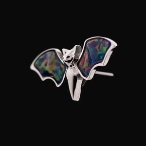 May include: A silver bat earring with iridescent opal wings. The wings have a dark blue, green, and purple color.