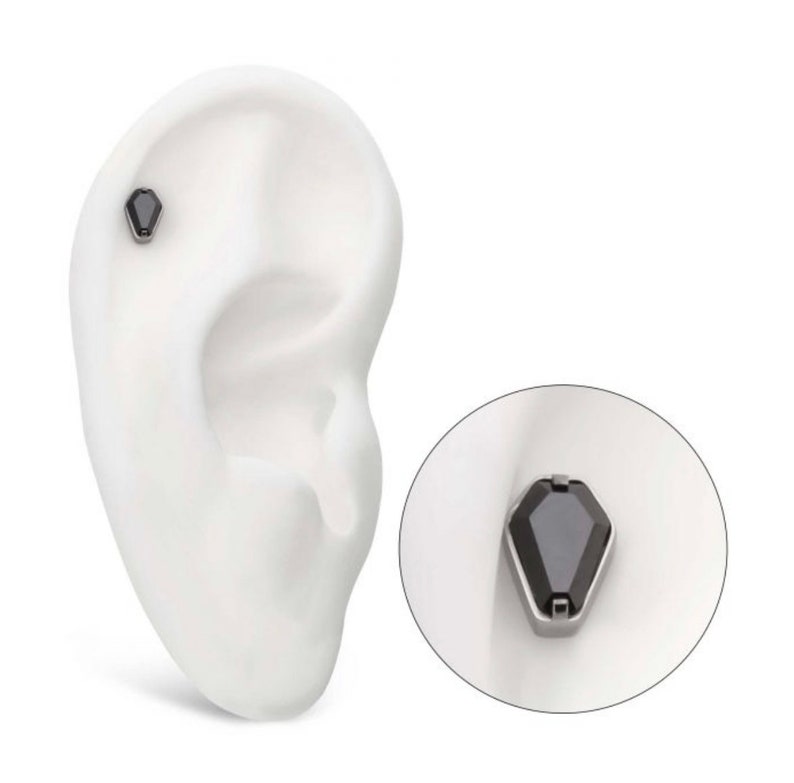 May include: A black gemstone ear cuff with a silver setting. The ear cuff is shown on a model ear.