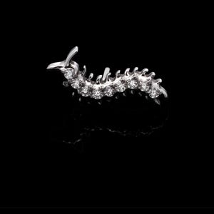 May include: A silver-toned brooch shaped like a segmented caterpillar, featuring a series of small, clear, round-cut stones set along its curved body. The piece has a metallic finish and a reflective surface, capturing light across its detailed form.