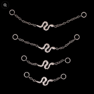 May include: Four silver-toned snake-shaped body jewelry pieces. Each piece features a detailed snake design connected to a chain with a ring at each end. The jewelry is set against a black background.