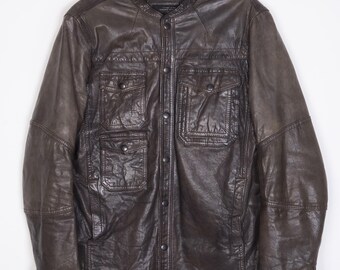 Puede incluir: Una chaqueta de cuero marrón con cierre de botones y varios bolsillos. La chaqueta tiene un cuello alto y mangas largas.