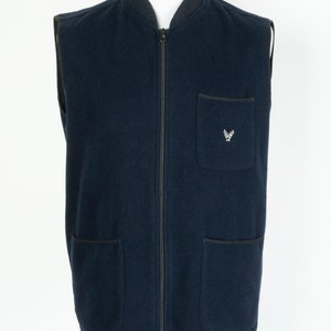 May include: A navy blue sleeveless zip-up vest with a small embroidered logo on the left chest. The vest has two large pockets on the bottom and a smaller pocket on the left chest.