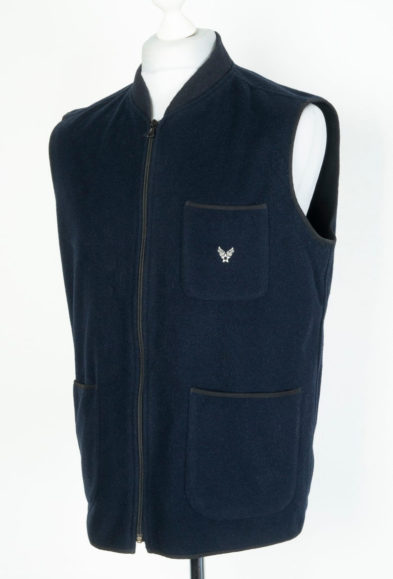May include: A navy blue fleece vest with a zipper closure and two front pockets. The vest has a small embroidered logo on the left chest.