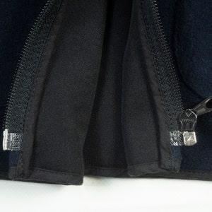 May include: Close-up of a black zipper on a dark blue jacket. The zipper is open and the fabric is folded back.