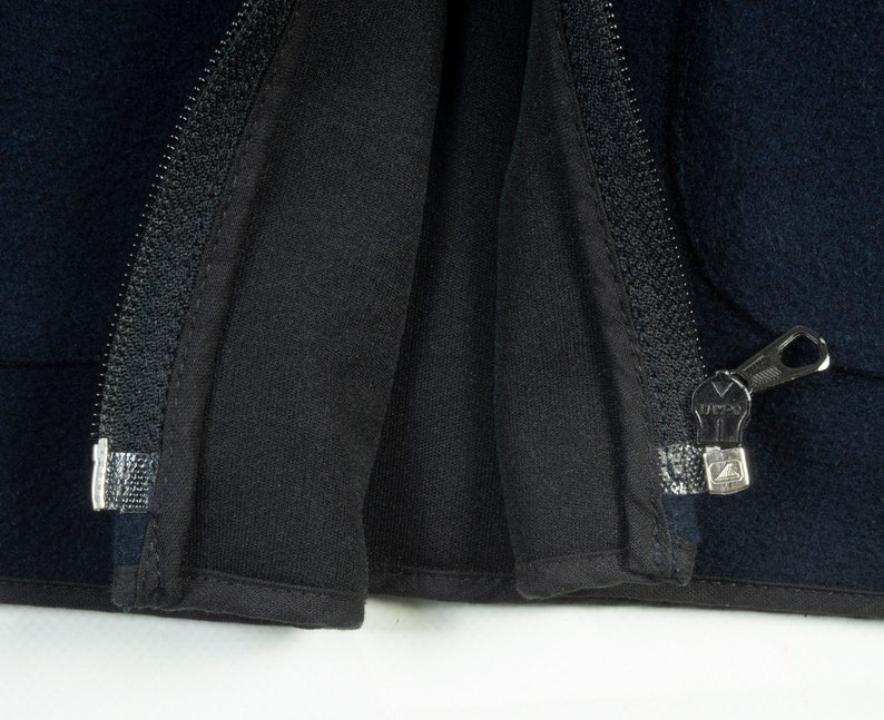 May include: Close-up of a black zipper on a dark blue jacket. The zipper is open and the fabric is folded back.