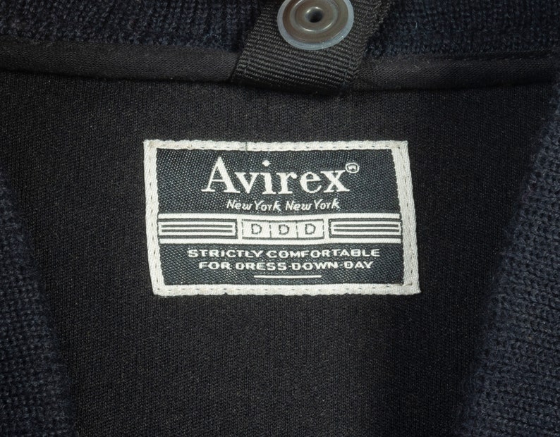 May include: A black Avirex label with white text that reads "Avirex", "New York, New York", "DDD", and "Strictly Comfortable for Dress-Down Day".